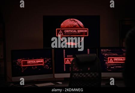 Workplace of IT engineer or software developer in dark server room with group of computer screens showing critical error in working process Stock Photo