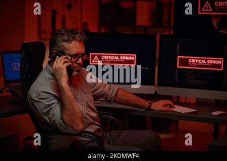 Serious mature programmer or director of large modern IT support department or company talking on mobile phone in server room Stock Photo