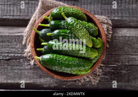 Fresh cucumbers in bowl on a wooden background, top view Stock Photo