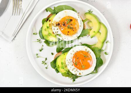 Bread with fried eggs, avocado and greens over light stone background.  Healthy breakfast. Top view, flat lay Stock Photo