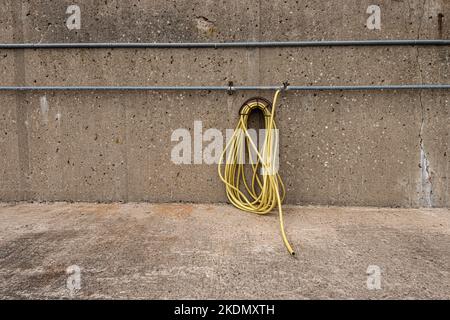 Yellow water hose hanging off a concrete wall. Stock Photo