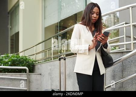 Elegant businesswoman walking down street and checking notifications on smartphone Stock Photo