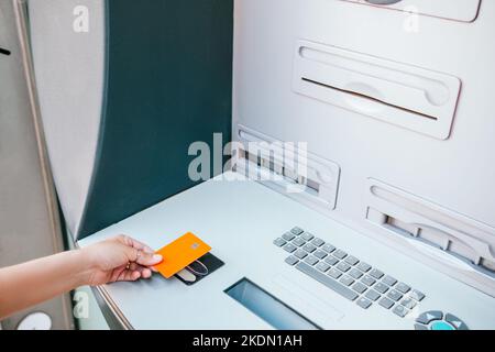 From above anonymous female holding blank credit card over contactless terminal on modern ATM while withdrawing money on city street Stock Photo