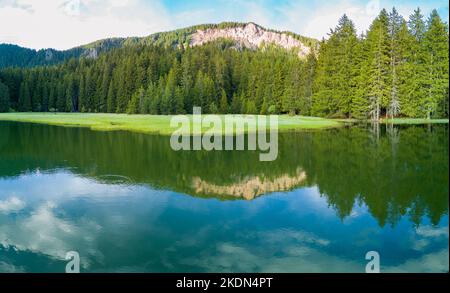 Intermountain azure lake with shores covered with vegetation against backdrop of silhouettes of Rhodope mountains and clouds. Panorama, top view Stock Photo