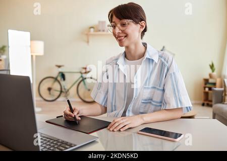 Portrait of smiling young woman using pen tablet at home office workplace for digital design or photo editing Stock Photo