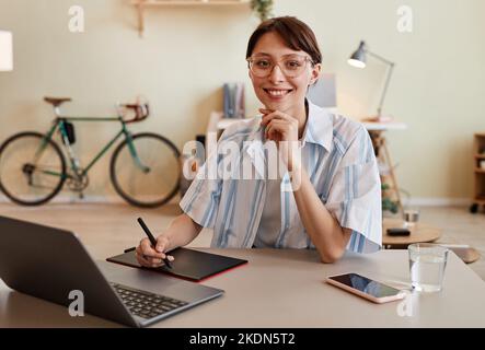 Portrait of young female designer smiling at camera and using pen tablet at home office workplace Stock Photo