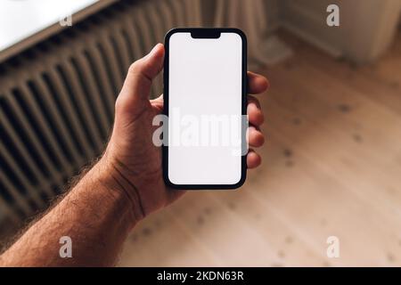 Blank mobile phone screen mockup in male hand, man using smartphone device in living room, selective focus Stock Photo