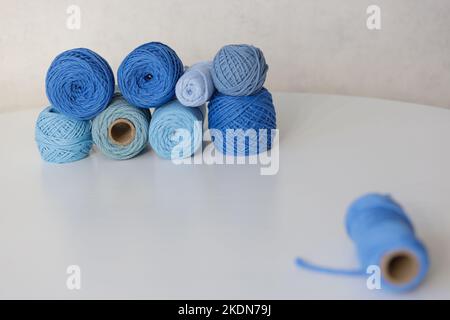 Blue balls for macrame are laid out on a white table. One ball out of focus in the foreground Stock Photo