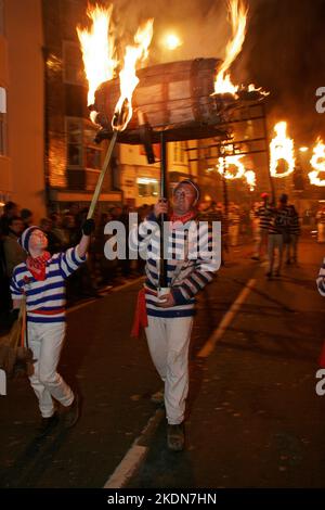 Jason Winter, Captain of Tar Barrels for Borough, carries a flaming barrel as a smuggler lights a Roman Candle in the main procession of the evening. Stock Photo