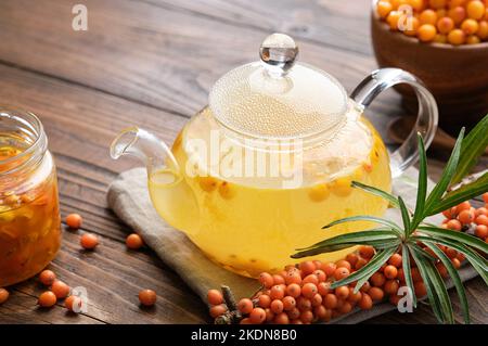 Glass tea kettle of healthy sea buckthorn tea, a sprig of buckthorn berries, jar of sea buckthorn jam. Natural edible remedies to strengthen the immun Stock Photo