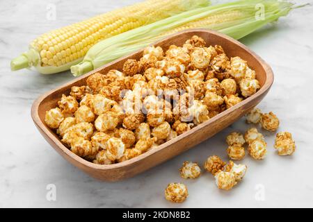 Wooden bowl of caramel popcorn, fresh corncobs on background. Stock Photo