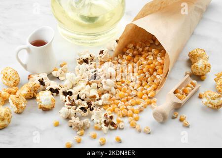 Popcorn, dried corn grains, caramel sauce and oil bottle on kitchen table. Stock Photo