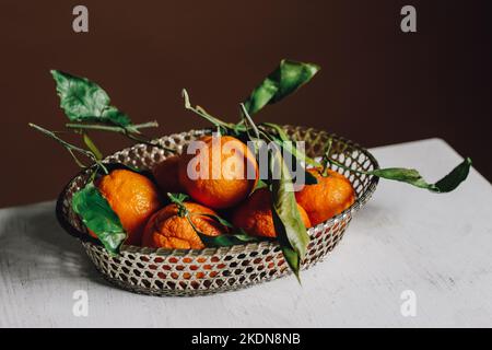 metal basket full of mandarin orange fruit with green leaves Stock Photo