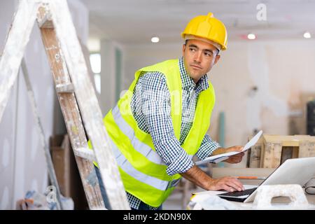 Engineer with drawings in his hands, checks the house reconstruction plan on a laptop Stock Photo