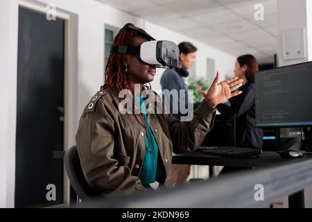 African american database admin working with virtual reality goggles to develop server app in it agency office, using source code. Checking programming language on cloud computing database, web developer. Stock Photo