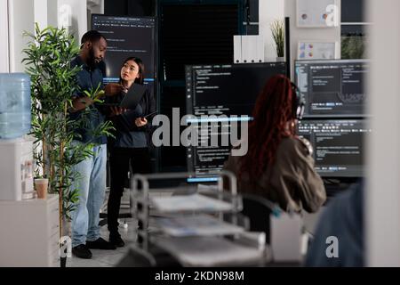 Two app developers analyzing html code looking for errors on laptop computer, checking big tv monitor in it agency office. Coders working on cyber security innovation in busy software company. Stock Photo