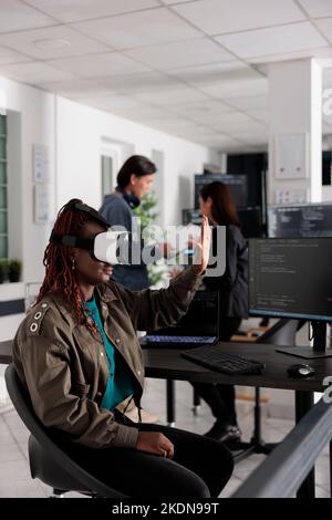 African american system engineer working with vr goggles to create programming server with html script on terminal window. System engineer using virtual reality headset to plan new interface. Stock Photo