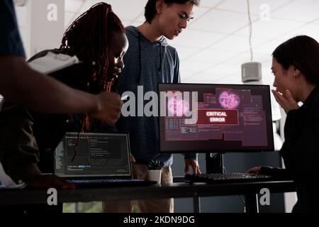 Team of software developers looking at monitor dealing with security breach alert on pc, trying to solve hacking and critical error. Engineers using terminal window and having system hacked crash. Stock Photo