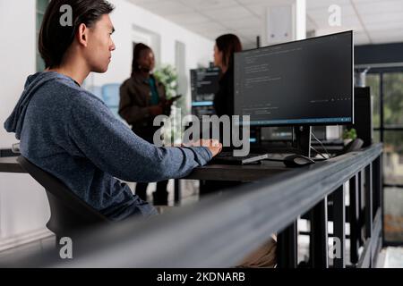 Asian programmer analyzing compiling html code on computer display, working on interface development. System developer using terminal window with firewall server data in it big data office Stock Photo