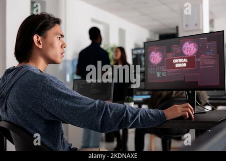 Worried software developer having web server hacked, looking at critical error on computer screen in programming office. Asian web developer trying to solve hacking problem, firewall security. Stock Photo