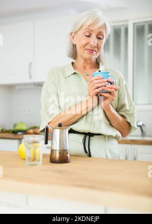 Cheerful senior woman having breakfast with cup of coffee Stock Photo