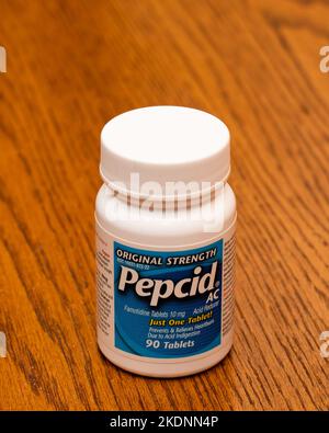 A white plastic bottle of Pepcid AC tablets for heartburn, acid indigestion and upset stomach on a wooden desk. Stock Photo