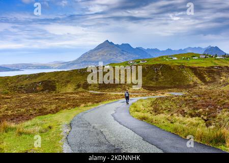 A walker on the moorland road heading down to Elgol, Isle of Skye, Scotland, UK. The Cuillin mountains in the distance. Stock Photo