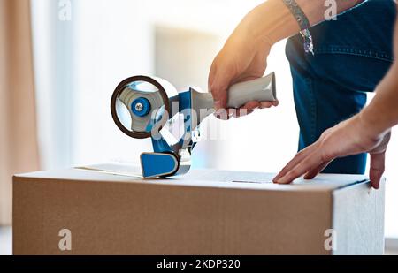 These are exciting times. an unrecognizable young man closing a cardboard box with tape at home. Stock Photo
