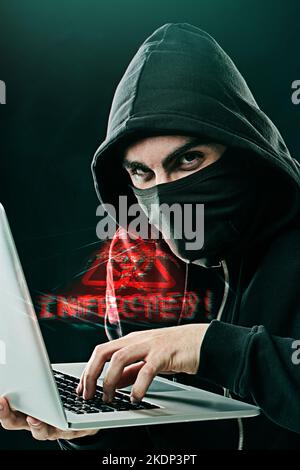 Someone is in for a nasty surprise. Portrait of a computer hacker using a laptop while standing against a dark background. Stock Photo