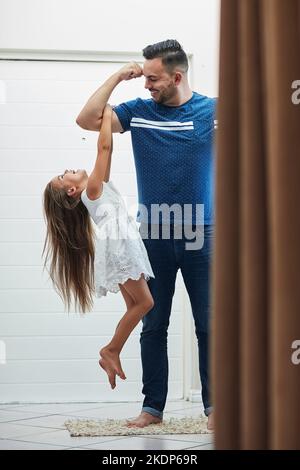 Youve got some super strength, Dad. a little girl holding on to her fathers arm as he lifts her up. Stock Photo