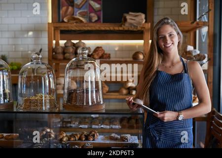 Its been a successful day so far. Portrait of a young business owner using a digital tablet in her bakery. Stock Photo