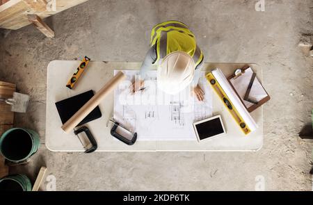 Engineering, building and aerial of construction worker with blueprint, tools and digital tablet on desk. Architect check engineering design Stock Photo