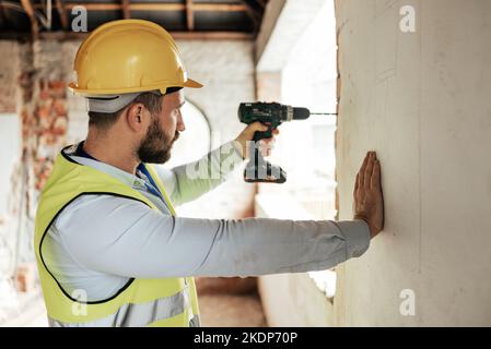 Construction worker, man or drilling wall with electric tool for utility lines, pipes or duct work in office building property. Engineering worker or Stock Photo