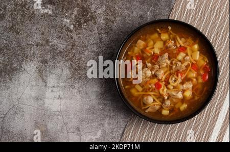 Pork Noodle Soup with potatoes and pepper in a bowl on a dark background. Top view, flat lay Stock Photo