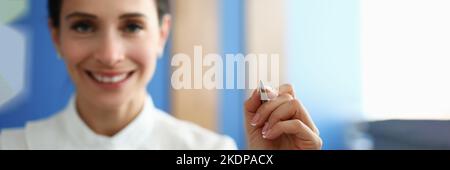 Smiling woman holding pen and writing in air Stock Photo