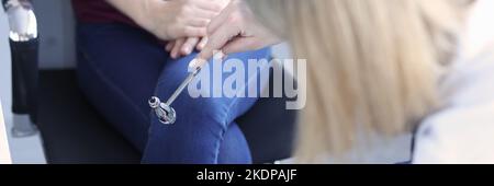 Doctor neurologist checking knee reflexes of female patient using percussion hammer in clinic Stock Photo