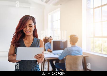 Must have technology for managing a productive office. a young entrepreneur using a digital tablet at work with her team in the background. Stock Photo
