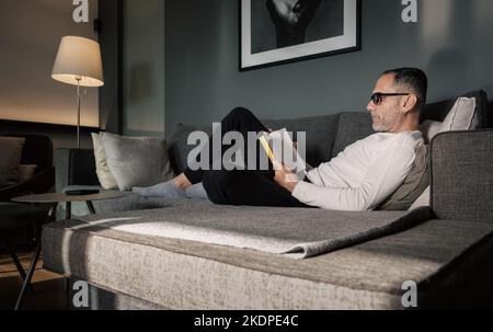Man reading book on couch. Stock Photo