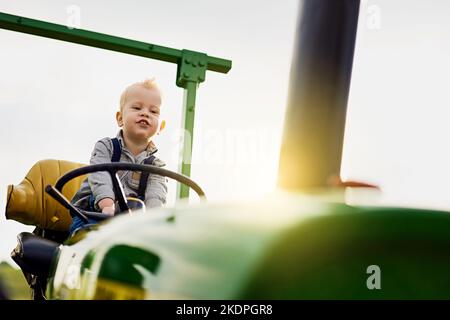 Old MacDonald had a son. an adorable little boy riding a tractor on a farm. Stock Photo