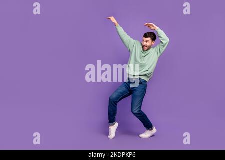Full body length photo of young impressed funny man wear stylish outfit tiptoe dancing hands up empty space shopping event isolated on purple color Stock Photo