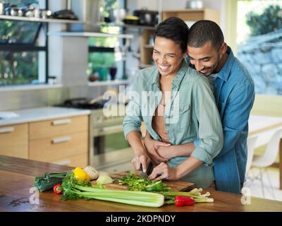 Is it getting hot in this kitchen...an affectionate young couple preparing a meal together in their kitchen. Stock Photo
