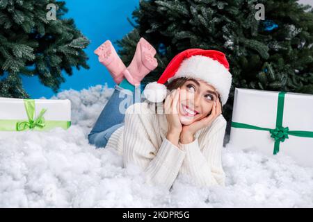 Full length photo of pretty lovely person laying snow hands touch cheeks dreamy pine tree isolated on blue color background Stock Photo