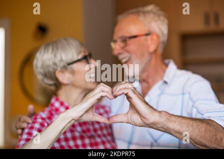 Happy senior couple is embracing and making heart shape with their hands. Stock Photo