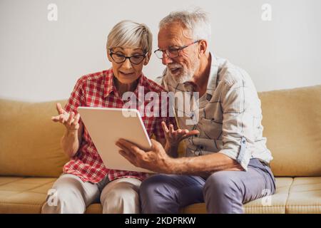 Senior couple sitting in living room and chatting with their family on digital tablet. Stock Photo