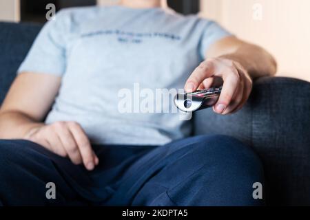 Tv remote in hand. Watching stream service in television sitting on sofa. Movie night. Man streaming series, film or news online. Change channel. Stock Photo