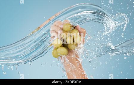 Hands with grapes, water splash and studio blue background of fruits sustainability, healthy lifestyle and juice detox, nutrition and vitamins. Bunch Stock Photo