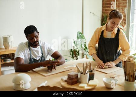 Warm toned portrait of young black man shaping clay while enjoying art class in pottery studio with tutor Stock Photo