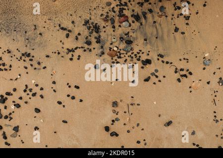 yellow beach sand with a little black sand and black rocks on it Stock Photo
