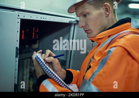 Making a note of the days results. a young engineer working with complicated machinery while wearing safety gear. Stock Photo