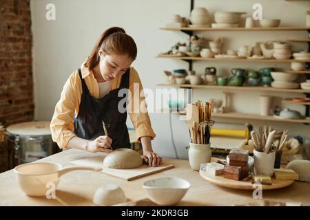 Warm toned portrait of young female artist shaping handmade ceramic bowl in pottery studio, copy space Stock Photo